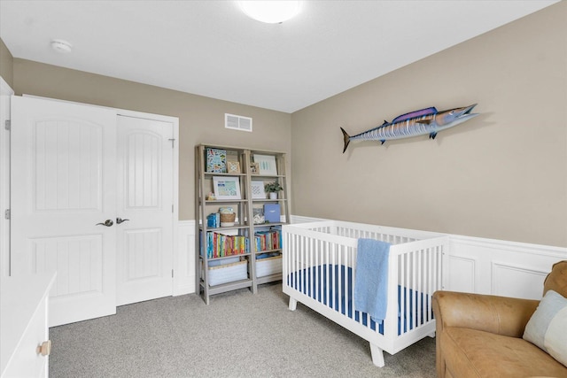 bedroom with wainscoting, visible vents, light carpet, and a closet