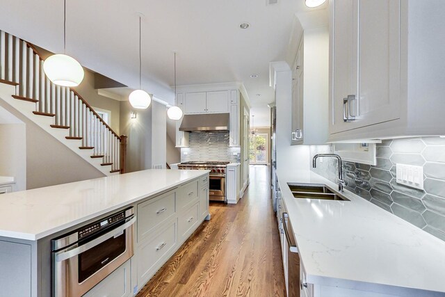 kitchen with a sink, high end range, light wood-type flooring, tasteful backsplash, and under cabinet range hood
