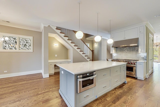 kitchen with light wood finished floors, appliances with stainless steel finishes, under cabinet range hood, and tasteful backsplash