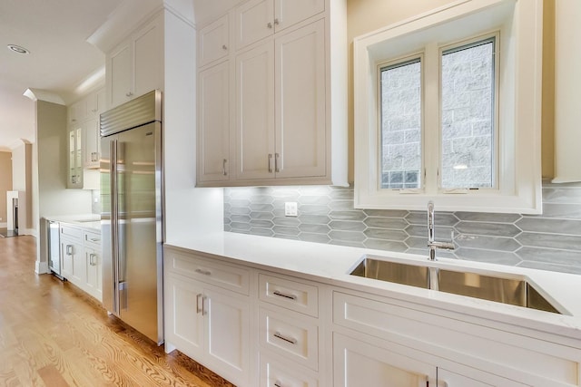 kitchen with backsplash, a sink, light countertops, beverage cooler, and stainless steel built in refrigerator