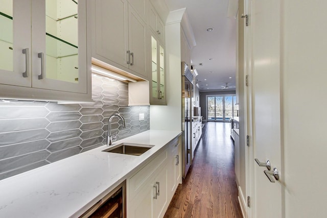 kitchen featuring dark wood-style flooring, light stone counters, a sink, decorative backsplash, and glass insert cabinets