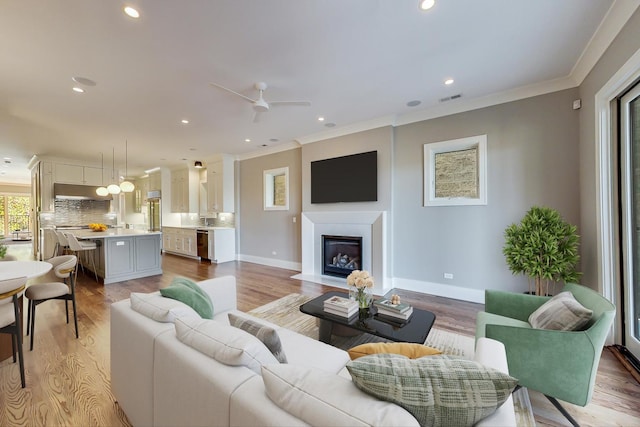 living room featuring recessed lighting, visible vents, ornamental molding, and a glass covered fireplace