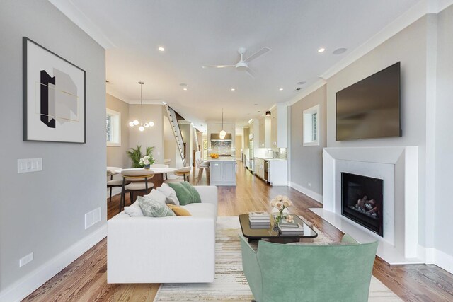 living room featuring ceiling fan, visible vents, a fireplace, baseboards, and ornamental molding