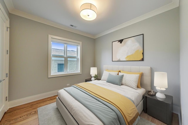 bedroom with baseboards, ornamental molding, light wood finished floors, and visible vents