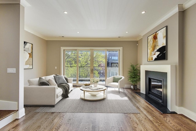 living room with crown molding, a glass covered fireplace, wood finished floors, baseboards, and recessed lighting