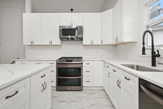 kitchen featuring white cabinets, stainless steel appliances, a sink, and marble finish floor