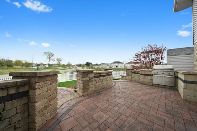 view of patio / terrace with an outdoor kitchen, fence, a residential view, and a grill