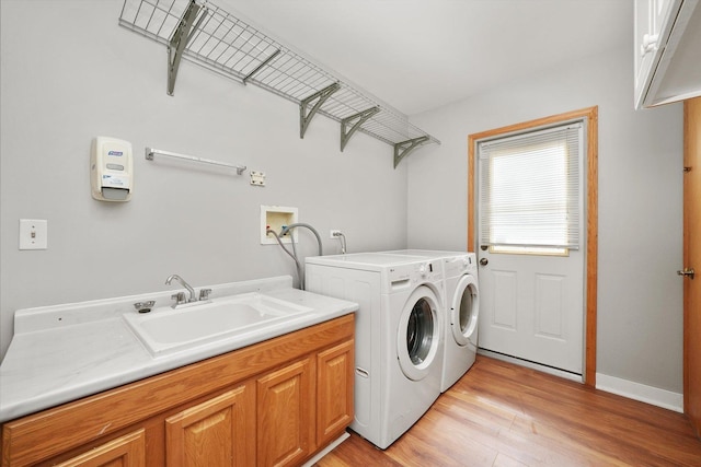 laundry area with cabinet space, washing machine and clothes dryer, a sink, light wood finished floors, and baseboards