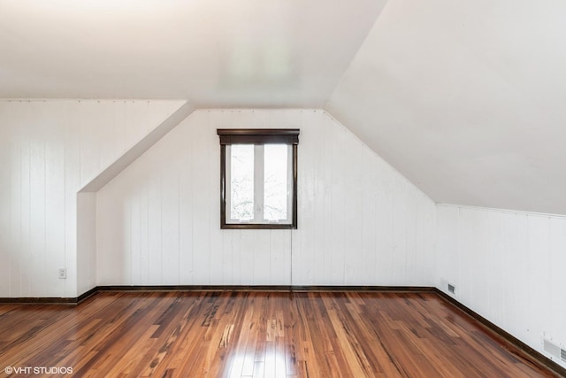 additional living space featuring wood walls, visible vents, vaulted ceiling, and wood-type flooring
