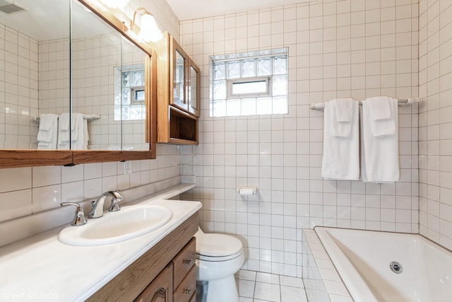 bathroom with tile walls, vanity, tiled tub, toilet, and visible vents