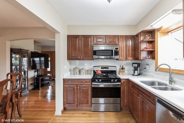 kitchen with light wood-style floors, stainless steel appliances, arched walkways, and a sink
