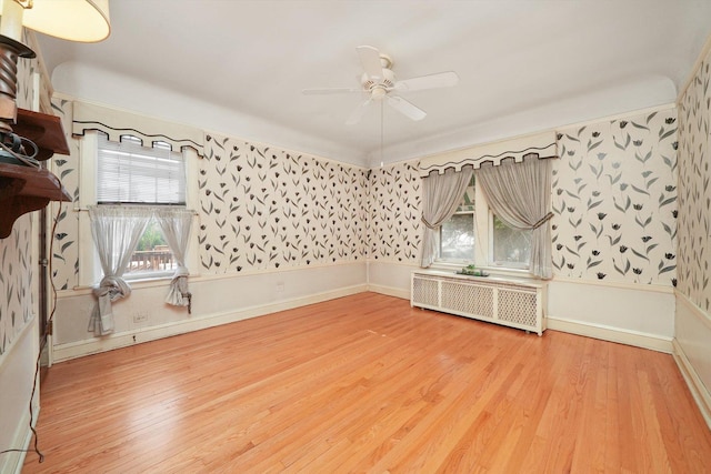spare room with radiator heating unit, a ceiling fan, wood finished floors, and a wealth of natural light
