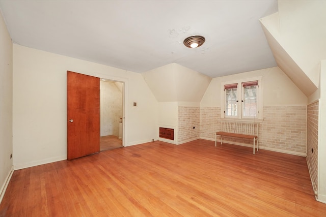 additional living space featuring baseboards, vaulted ceiling, light wood finished floors, and brick wall