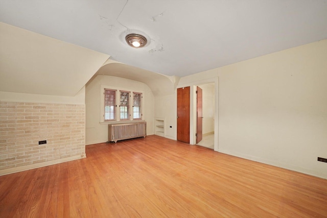 bonus room with baseboards, brick wall, radiator heating unit, and wood finished floors