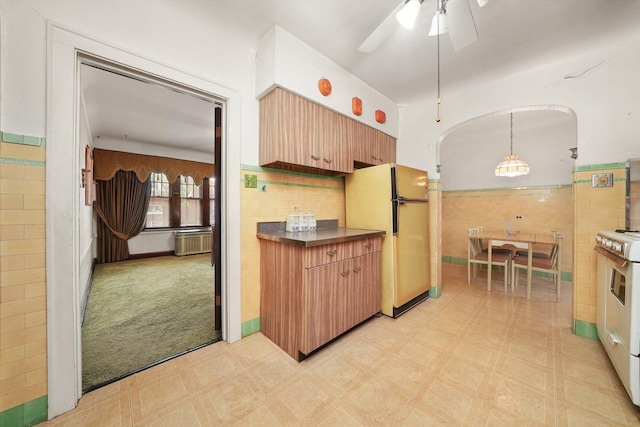 kitchen featuring ceiling fan, dark countertops, arched walkways, light floors, and white appliances