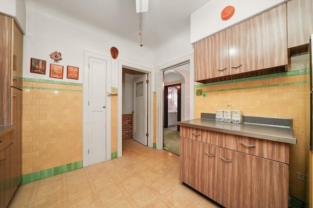 kitchen featuring dark countertops, arched walkways, a wainscoted wall, tile walls, and light floors