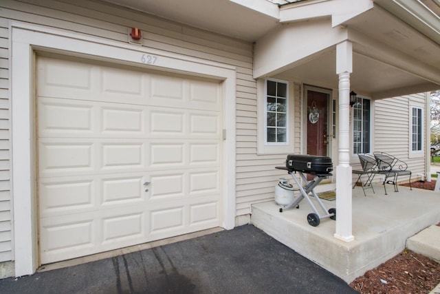 entrance to property with covered porch, a garage, and aphalt driveway