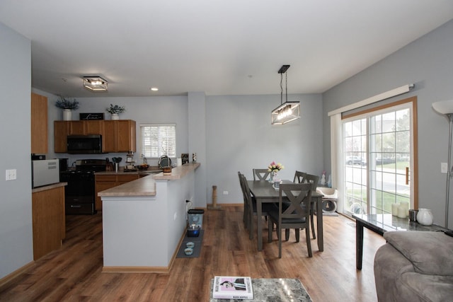 kitchen featuring a sink, brown cabinets, a peninsula, black range with gas cooktop, and wood finished floors