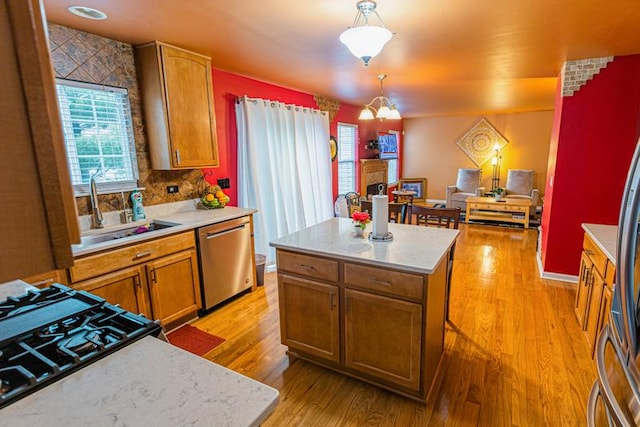 kitchen featuring stainless steel dishwasher, a sink, light wood-type flooring, light countertops, and a fireplace