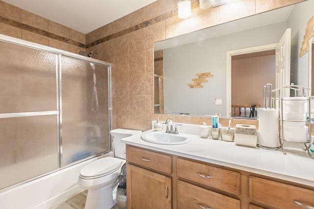 bathroom with tile walls, shower / bath combination with glass door, vanity, and toilet