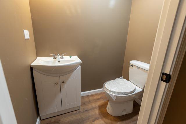half bathroom featuring vanity, toilet, wood finished floors, and baseboards