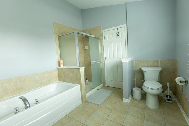 bathroom featuring tile patterned flooring, a garden tub, a shower stall, toilet, and tile walls