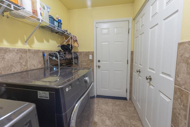 clothes washing area with washer and dryer, tile walls, and a wainscoted wall