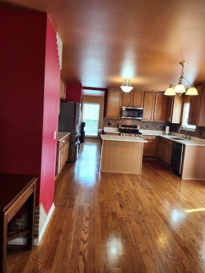 kitchen featuring appliances with stainless steel finishes, a sink, a center island, light countertops, and dark wood-type flooring