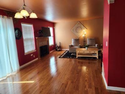 living room featuring wood finished floors, baseboards, a fireplace, and a chandelier
