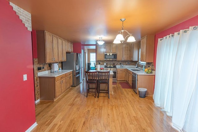 kitchen featuring stainless steel appliances, a sink, light wood finished floors, light countertops, and backsplash