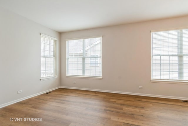 empty room featuring wood finished floors, visible vents, and baseboards