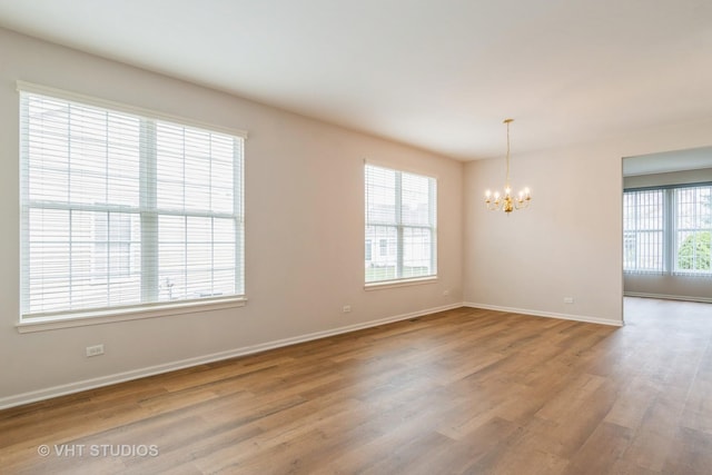 empty room with baseboards, a notable chandelier, and wood finished floors