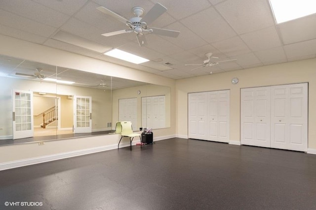 exercise area featuring baseboards, a ceiling fan, and a paneled ceiling