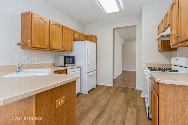 kitchen with a sink, light wood-style floors, white appliances, light countertops, and under cabinet range hood
