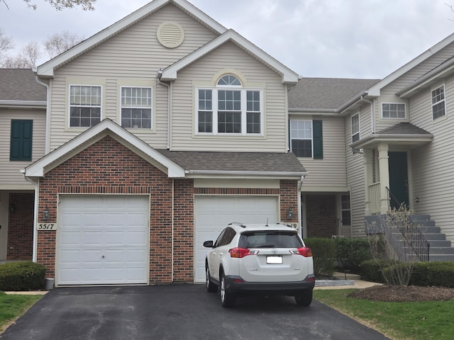 view of front of house with driveway, roof with shingles, brick siding, and a garage