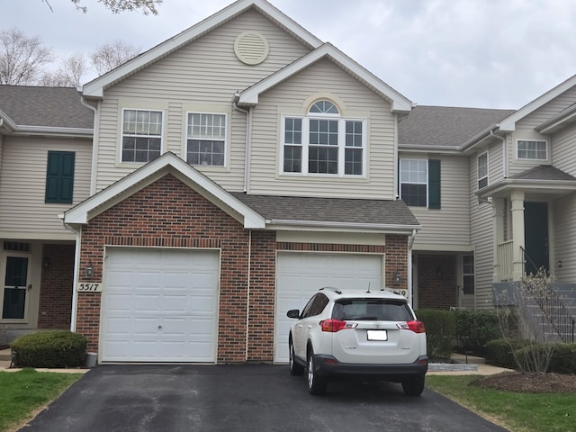 view of front of house with a garage, brick siding, driveway, and roof with shingles