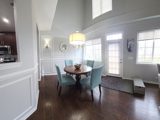 dining space featuring a chandelier, a high ceiling, dark wood-style flooring, and a decorative wall