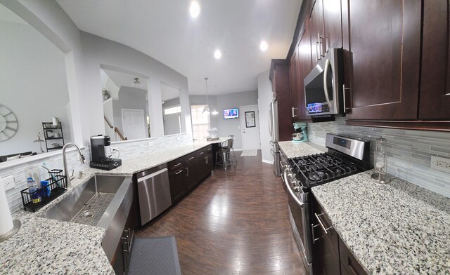 kitchen featuring light stone counters, decorative backsplash, stainless steel appliances, dark wood-style flooring, and a sink