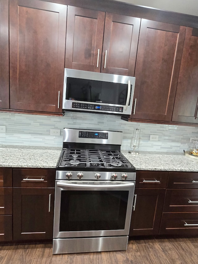 kitchen with dark wood finished floors, dark brown cabinets, backsplash, and appliances with stainless steel finishes