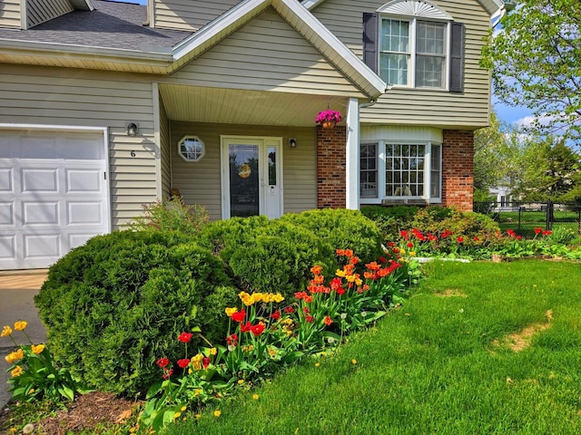 doorway to property featuring a lawn, fence, roof with shingles, brick siding, and an attached garage