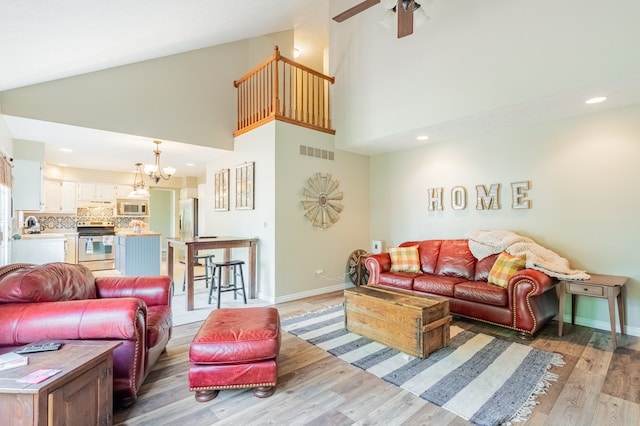 living room with light wood-style floors, high vaulted ceiling, ceiling fan with notable chandelier, and visible vents