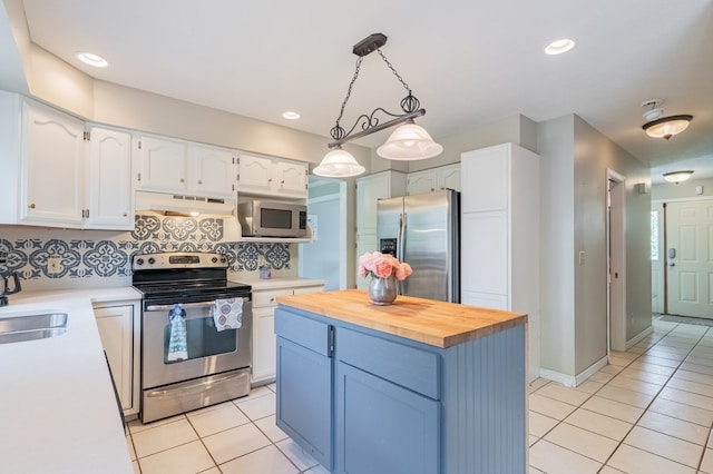 kitchen with appliances with stainless steel finishes, white cabinets, butcher block counters, under cabinet range hood, and light tile patterned flooring