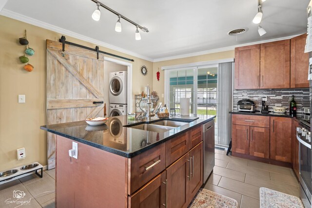 kitchen with track lighting, stainless steel dishwasher, stacked washer / dryer, a barn door, and a sink