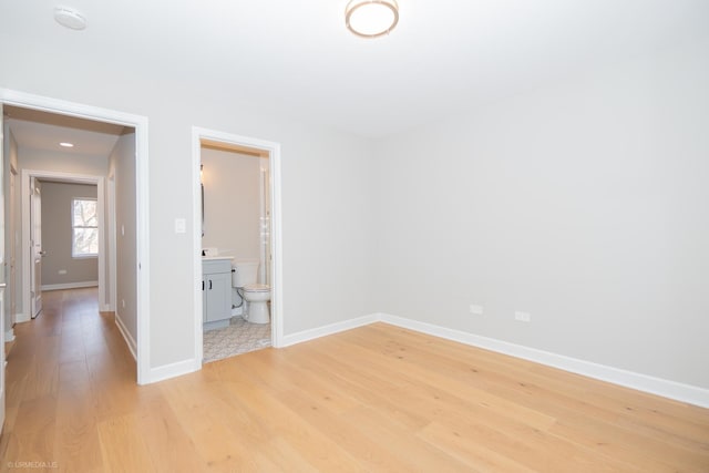 unfurnished bedroom featuring baseboards, ensuite bathroom, and light wood-type flooring