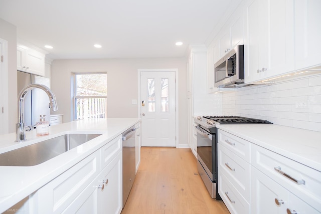 kitchen with a sink, light wood finished floors, appliances with stainless steel finishes, and white cabinets