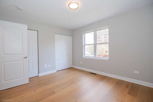 unfurnished bedroom with baseboards, multiple closets, visible vents, and light wood-type flooring