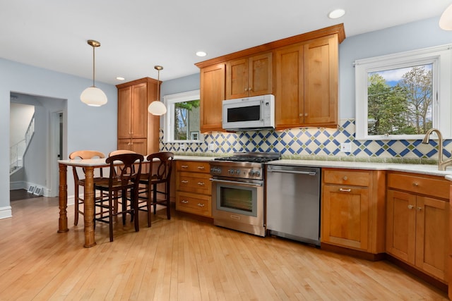 kitchen with backsplash, stainless steel appliances, light wood-type flooring, and light countertops