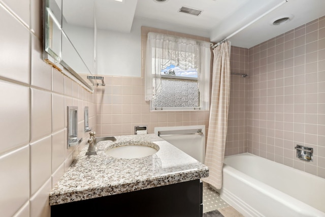 full bath with tile walls, visible vents, vanity, and shower / bath combo