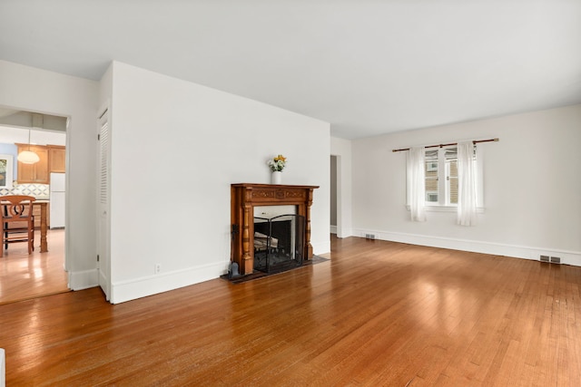 living room featuring a fireplace with flush hearth, wood finished floors, visible vents, and baseboards
