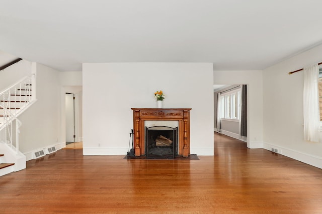 unfurnished living room with visible vents, wood finished floors, a fireplace, and stairs